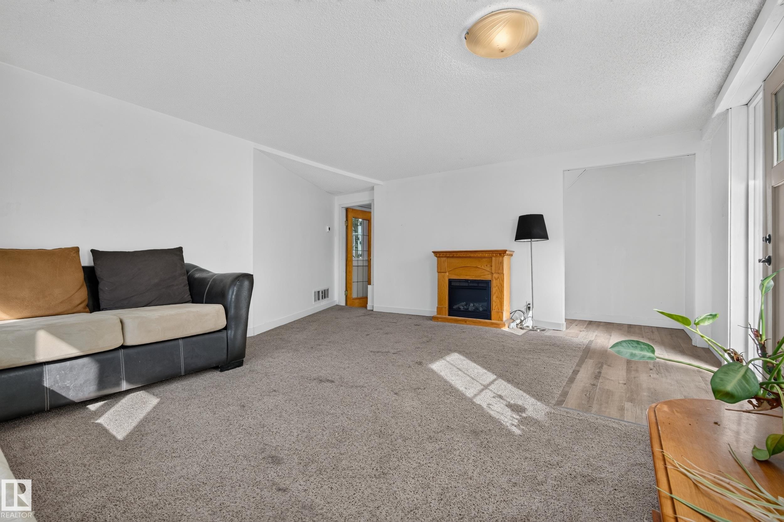 Carpeted living area with a wood-finish fireplace surround, recessed lighting, and a glass-paneled interior door - 11603 72 Avenue Nw, Edmonton, AB