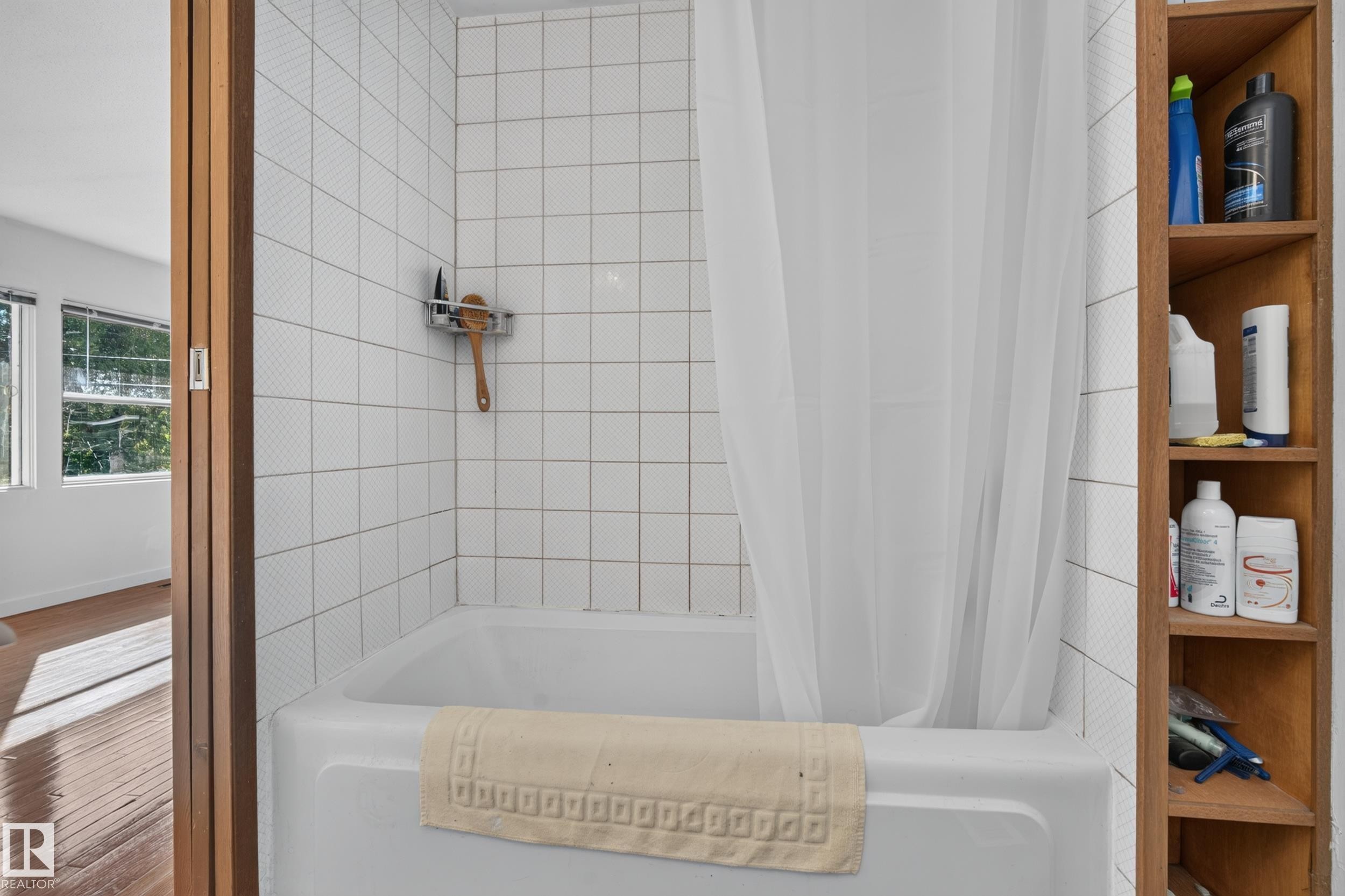 Bathtub with white tile surround, built-in wood shelving, and wood-paneled door frame - 11603 72 Avenue Nw, Edmonton, AB