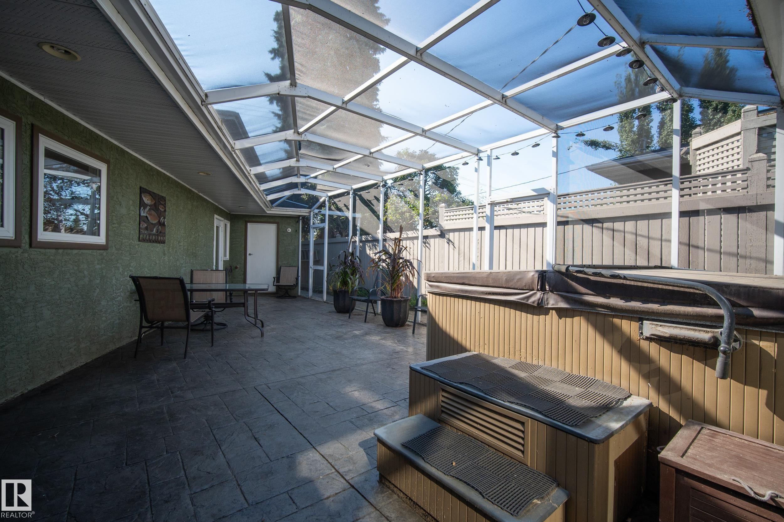 Enclosed patio with a transparent overhead structure, stamped concrete flooring, textured exterior wall, and a built-in outdoor spa - 11603 72 Avenue Nw, Edmonton, AB