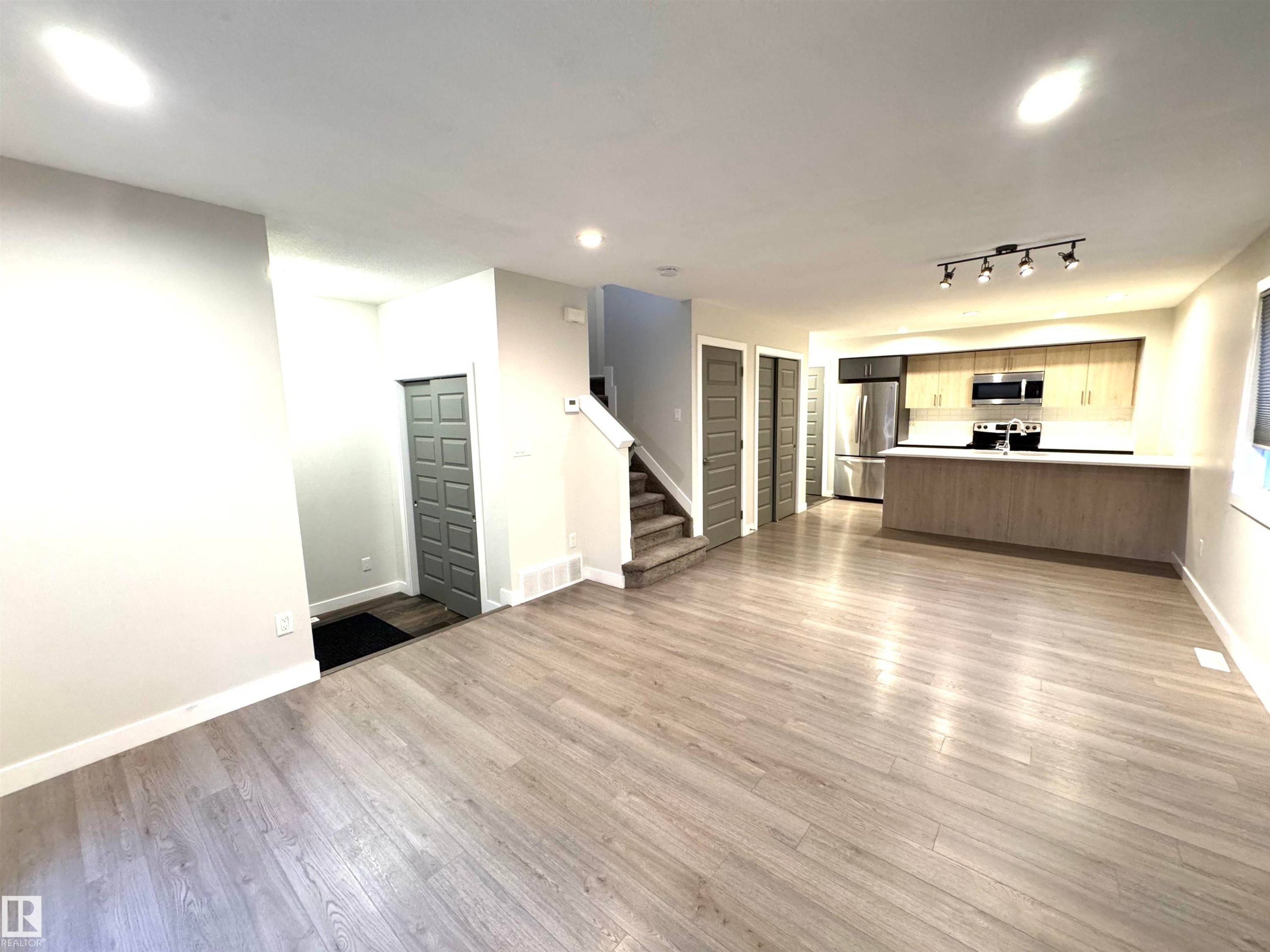 Light wood-finish flooring throughout, L-shaped kitchen island, stainless steel appliances, track lighting, and recessed ceiling lights - 12046 89 Street Nw, Edmonton, AB