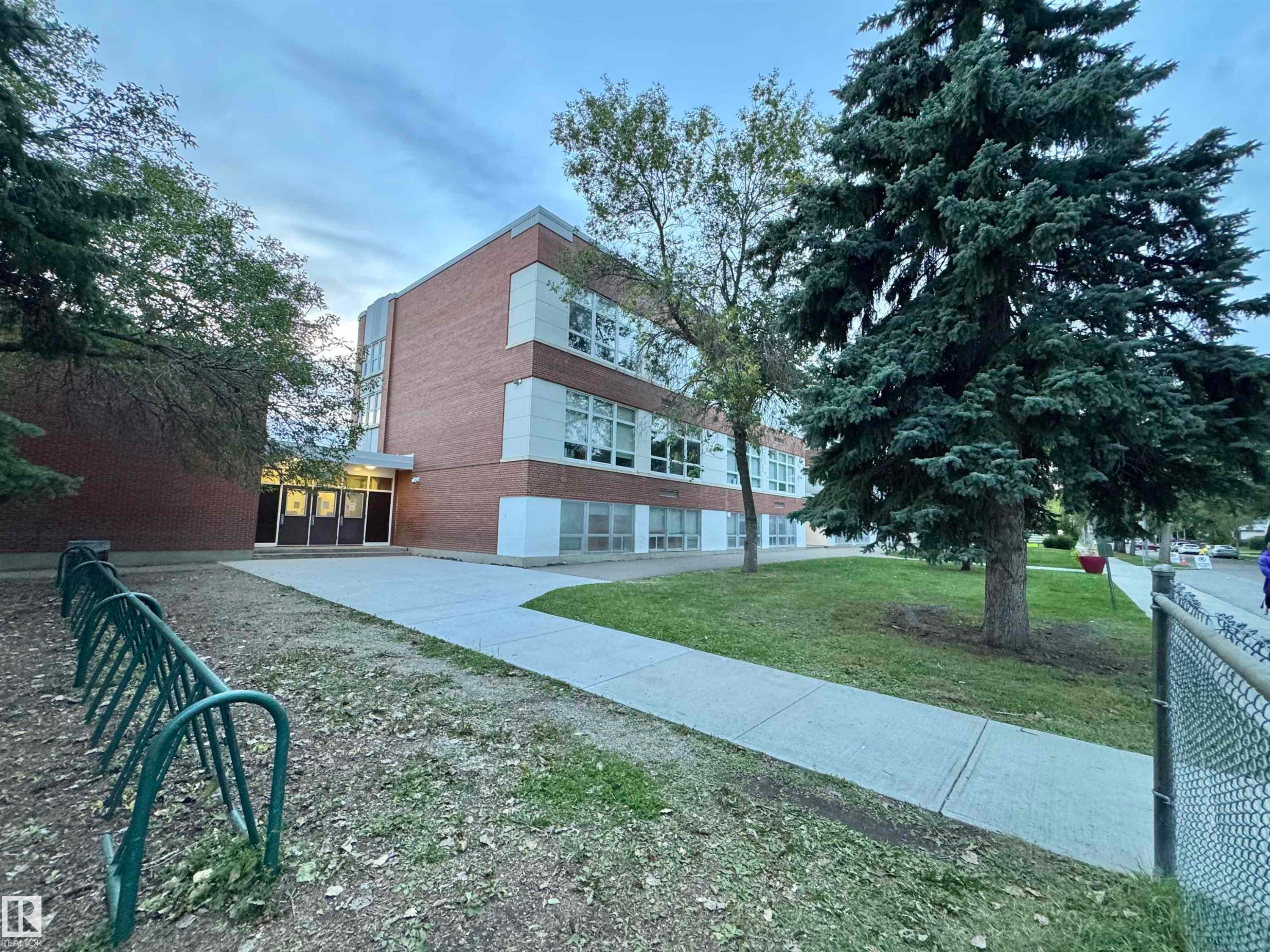 Brick exterior with multiple windows, concrete walkway, and mature trees - 12046 89 Street Nw, Edmonton, AB