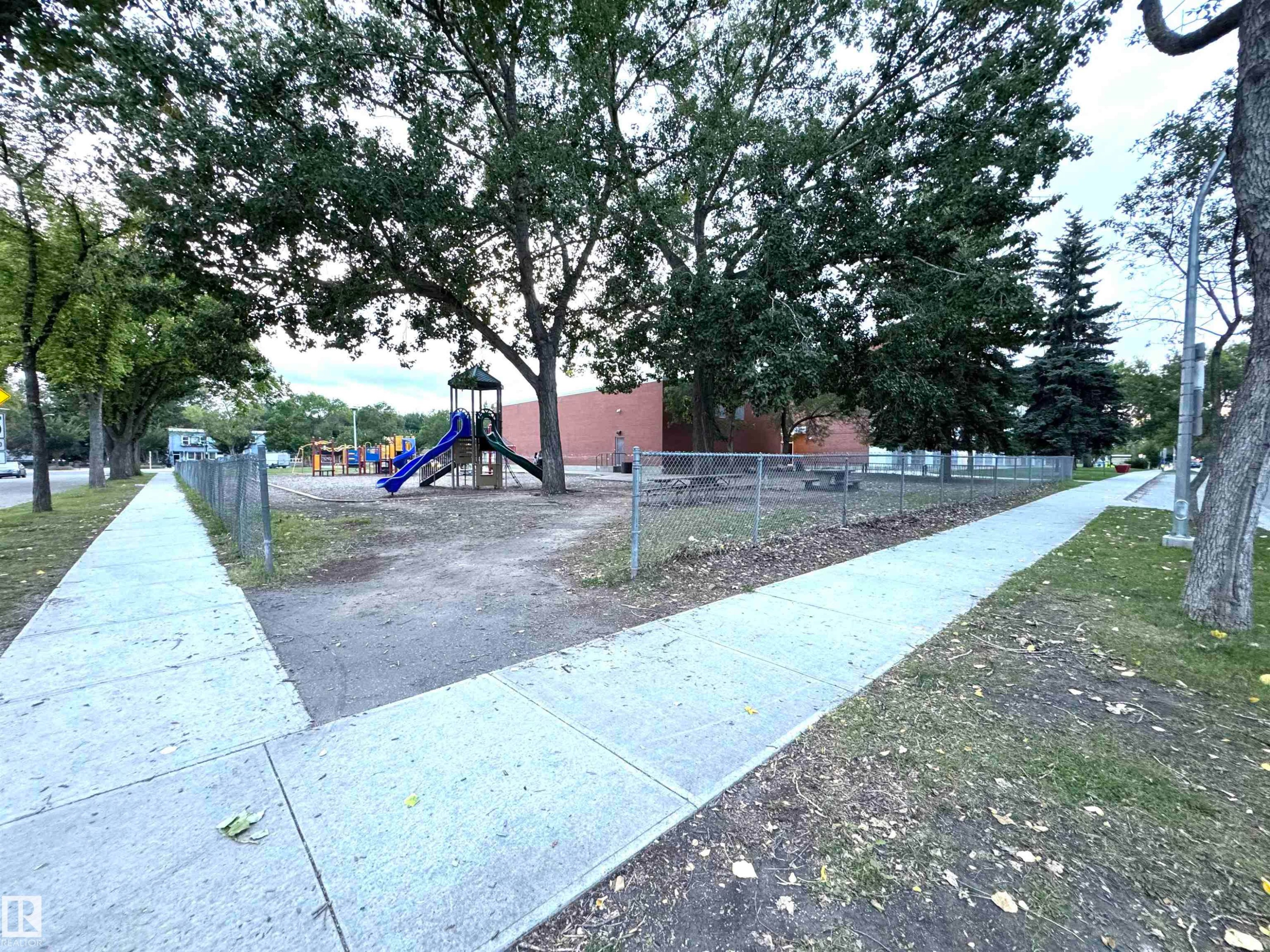 Gated recreational area featuring mature trees and a playground structure with slides - 12046 89 Street Nw, Edmonton, AB