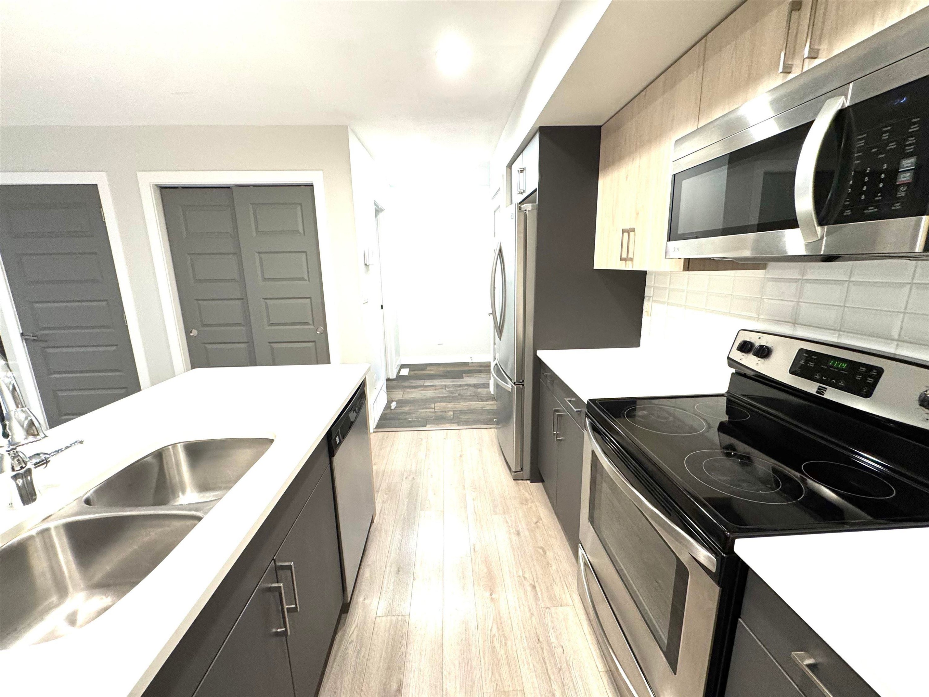 Contemporary kitchen featuring white countertops, stainless steel appliances, light wood-finish upper cabinetry, and a subway tile backsplash - 12046 89 Street Nw, Edmonton, AB