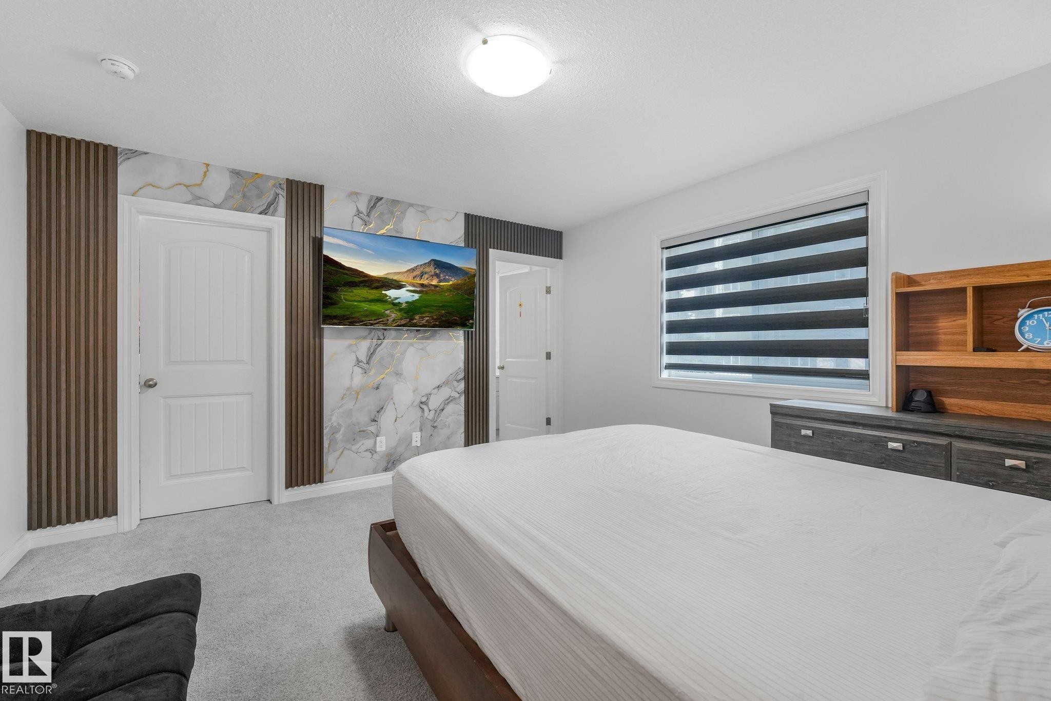 Wall-mounted television with marble-patterned accent wall, wood-finish slat details, and light gray carpeting - 12843 67 Street Nw, Edmonton, AB