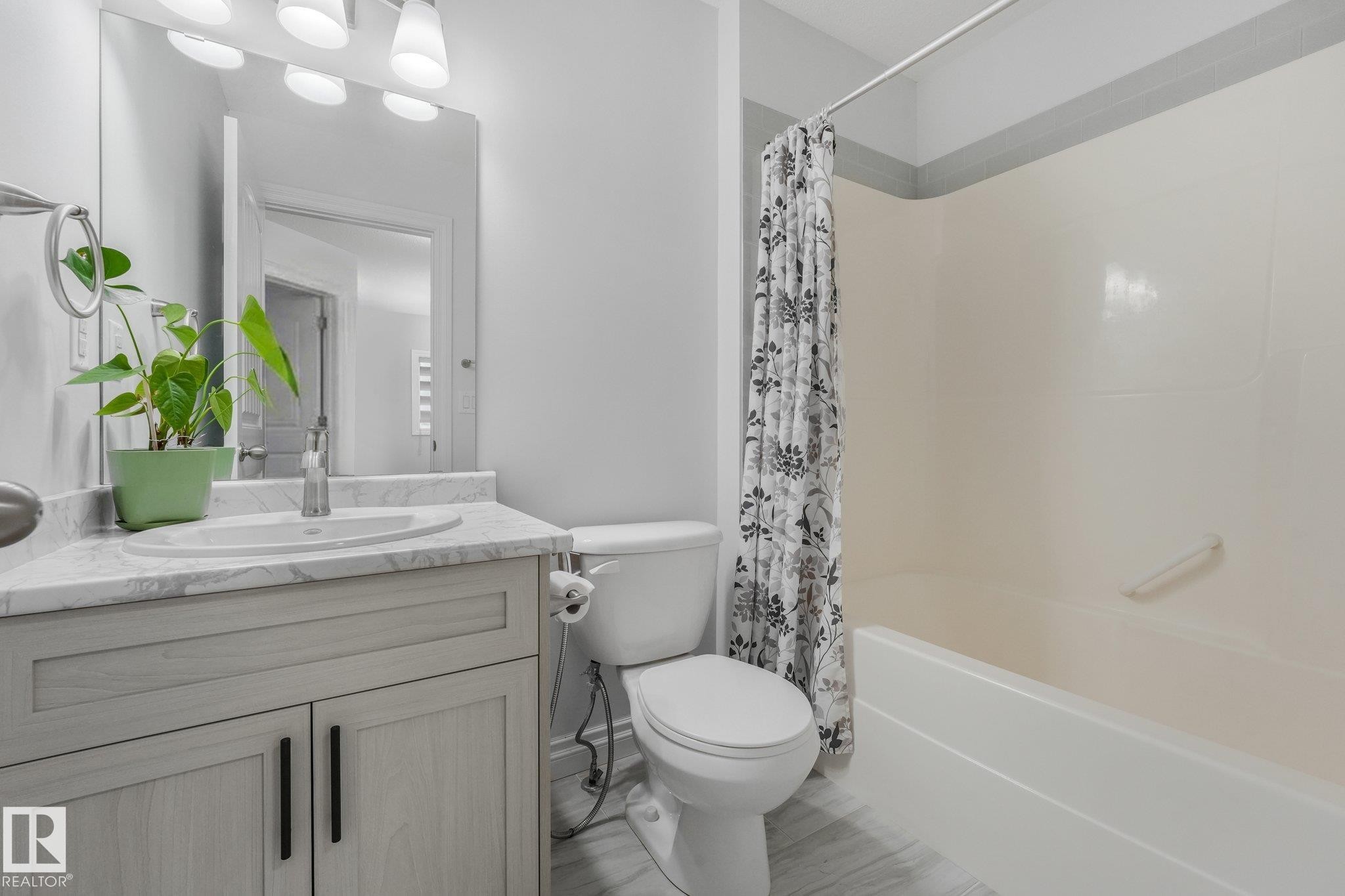 Bathroom featuring a vanity with a white countertop and undermount sink, a toilet, a shower-over-tub combination, and light wood-finish flooring - 12843 67 Street Nw, Edmonton, AB