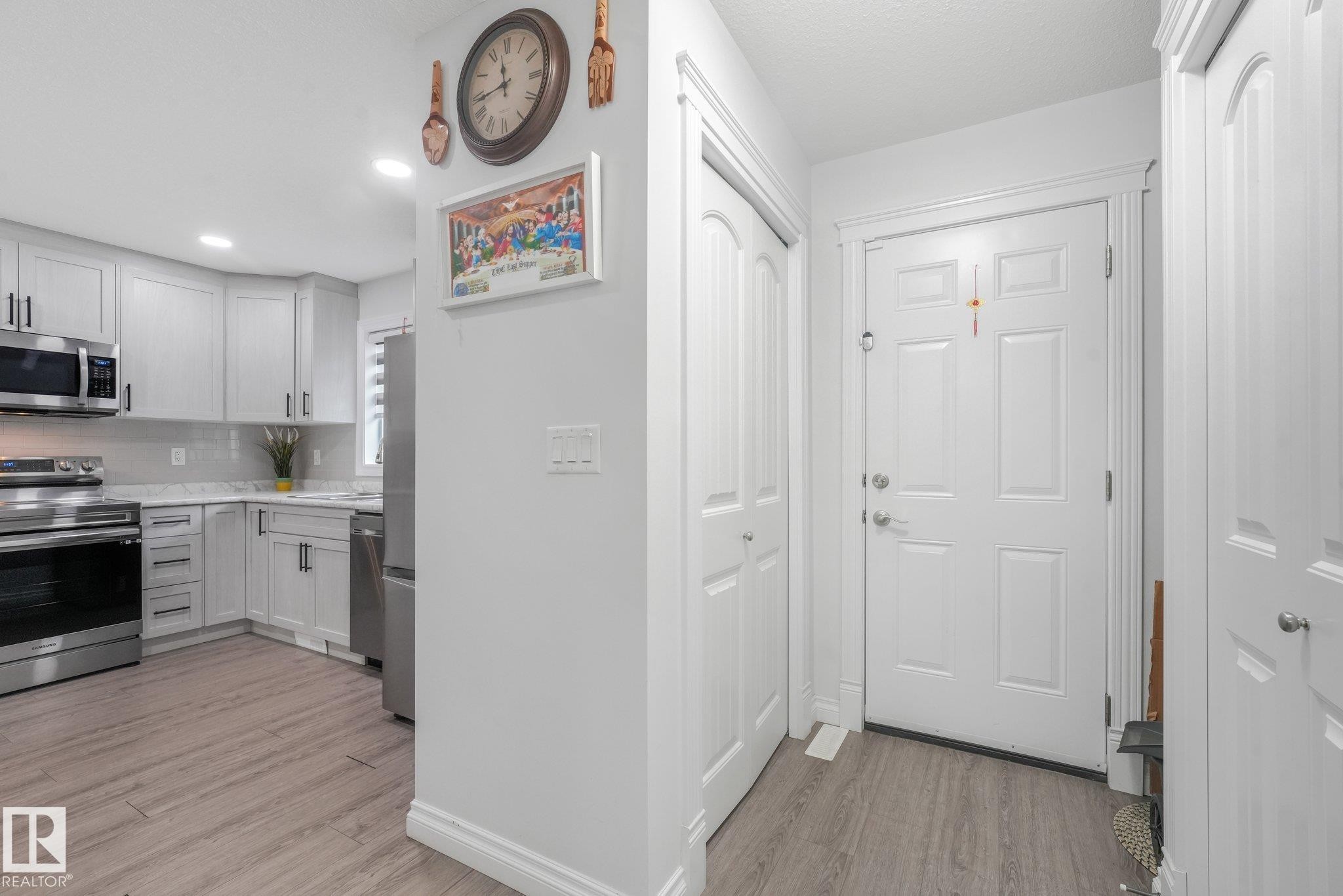 Wood-finish flooring throughout, bright white paneled entry door, recessed lighting, white shaker-style cabinetry, and stainless steel appliances - 12843 67 Street Nw, Edmonton, AB