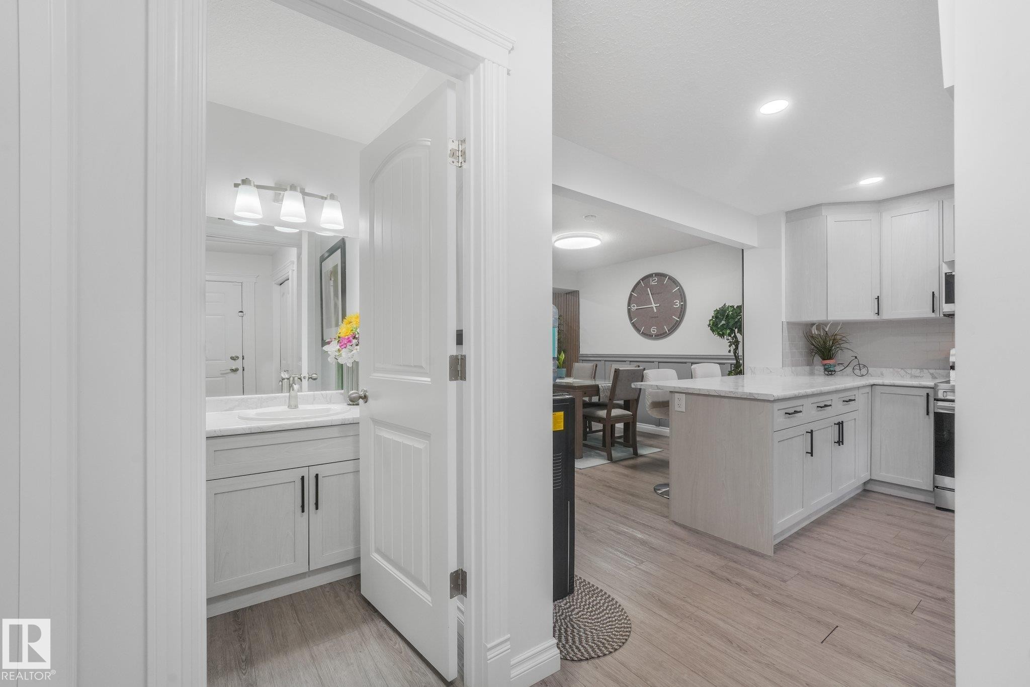 Modern kitchen featuring white cabinetry, a center island with countertop seating, and light wood-finish flooring - 12843 67 Street Nw, Edmonton, AB