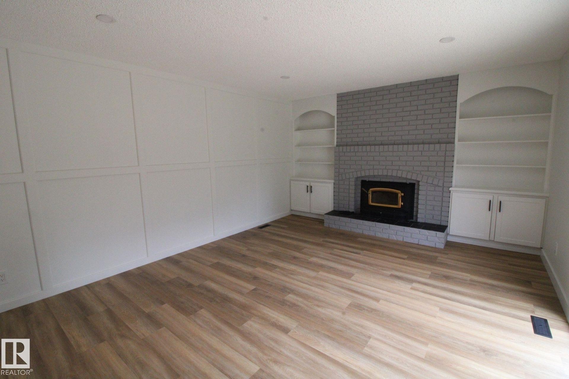 Wood-finish flooring, accent wall with paneling, brick-surround fireplace with hearth, and built-in shelving with cabinetry - 4224 110 Street Nw, Edmonton, AB