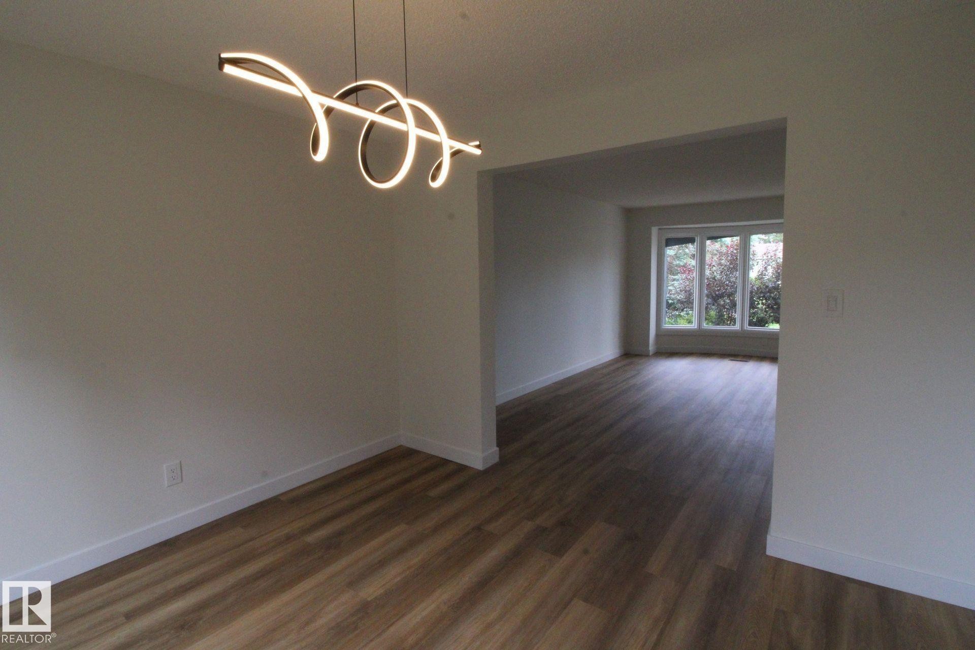 Open-concept interior featuring wood-finish flooring, a contemporary spiral chandelier, and a large window - 4224 110 Street Nw, Edmonton, AB