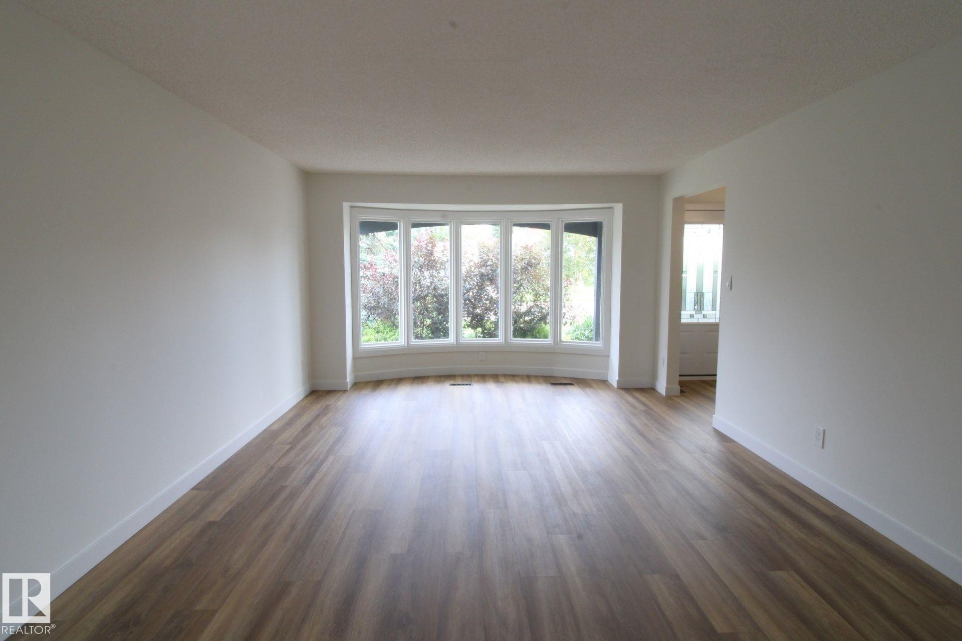 Spacious interior with neutral white walls, wood-finish flooring, and a curved bay window - 4224 110 Street Nw, Edmonton, AB