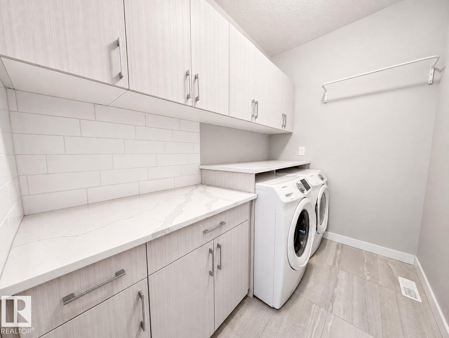 Full-size washer and dryer, tile flooring, solid surface countertops, extensive upper and lower cabinetry, and subway tile backsplash - 10516 76 Street Nw, Edmonton, AB