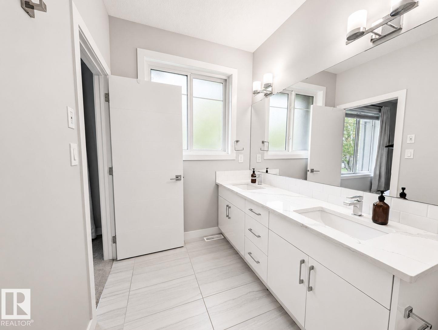 Dual vanity with integrated sinks and white countertops, under-vanity storage, large wall-mounted mirror, and tile flooring - 10516 76 Street Nw, Edmonton, AB