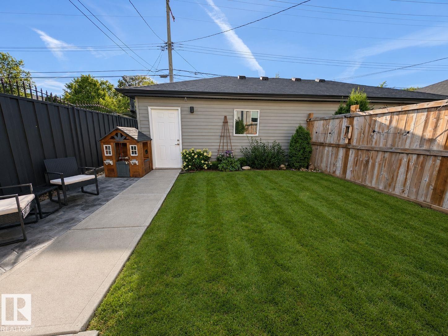 Expansive lawn area with a concrete pathway, privacy fencing, and a detached structure featuring siding and a white entry door - 10516 76 Street Nw, Edmonton, AB