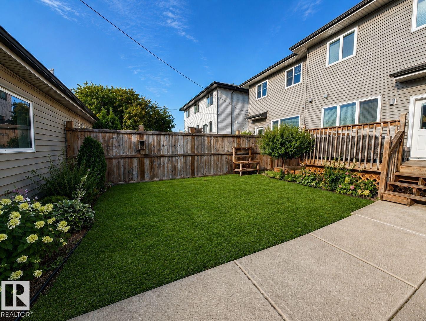 Manicured lawn with perimeter landscaping, wood fencing, a wooden deck, and concrete hardscaping - 10516 76 Street Nw, Edmonton, AB