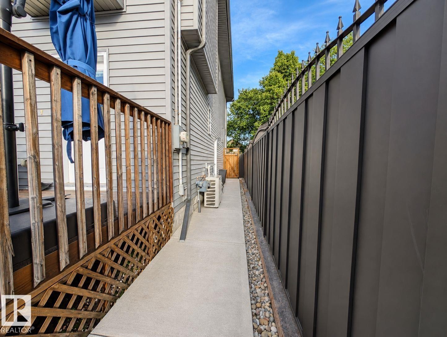 Siding exterior featuring a side concrete path, a wood deck with lattice skirting, and a tall privacy fence with decorative metal accents - 10516 76 Street Nw, Edmonton, AB