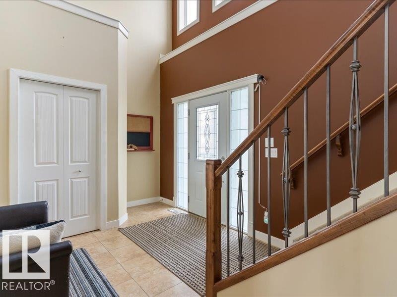Two-story foyer with transom and sidelight windows, tile flooring, wood and wrought iron staircase, and bi-fold panel door - 496 Ravine Court, Devon, AB
