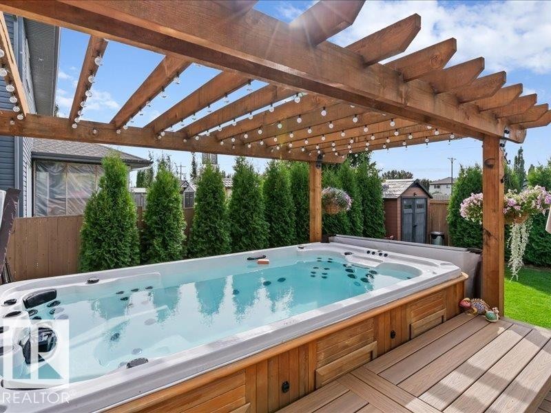 Expansive spa deck featuring a swim spa, wood pergola, string lighting, and composite decking - 496 Ravine Court, Devon, AB