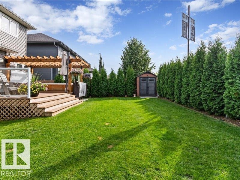 Expansive green space featuring a multi-level wood deck, a wood pergola, and a storage shed - 496 Ravine Court, Devon, AB