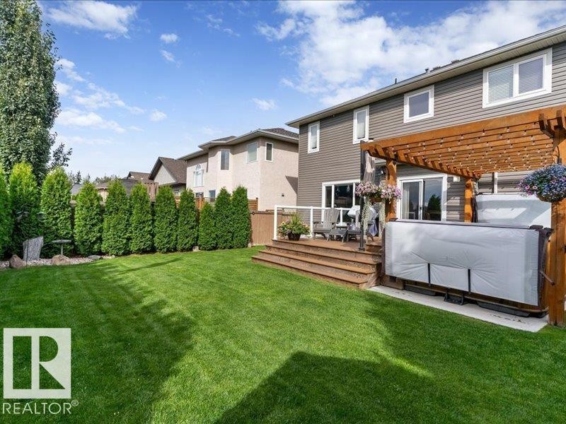 Expansive green lawn with mature evergreen trees, leading to a multi-level wooden deck - 496 Ravine Court, Devon, AB