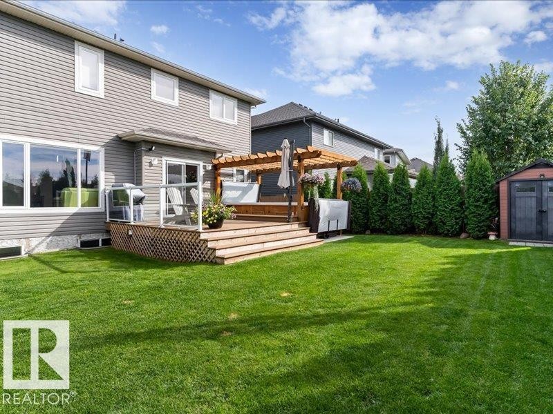 Expansive backyard featuring a large wooden deck with a pergola, mature privacy trees, and a storage shed - 496 Ravine Court, Devon, AB