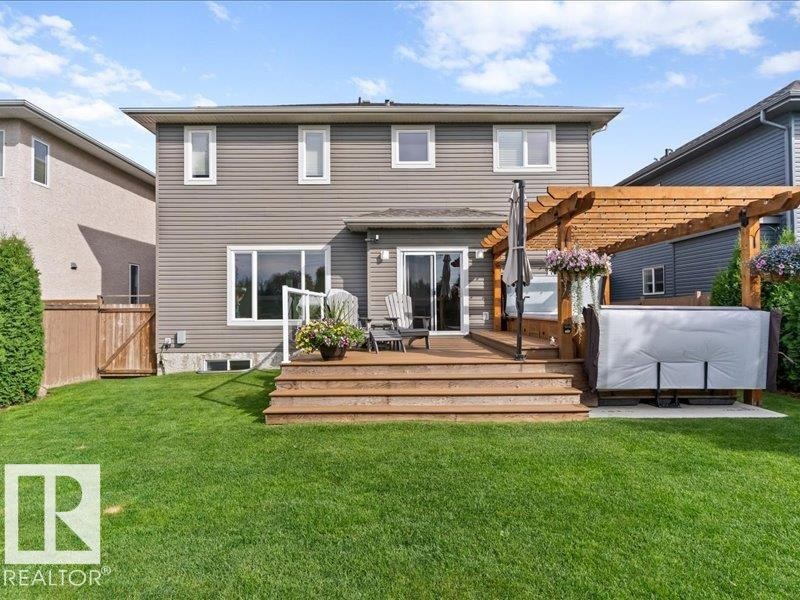 Expansive green lawn with a multi-level wood deck, glass railing, and a wood pergola - 496 Ravine Court, Devon, AB