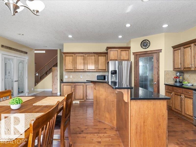 Kitchen featuring wood-finish cabinetry, black countertops, stainless steel appliances, and a tiled backsplash - 496 Ravine Court, Devon, AB