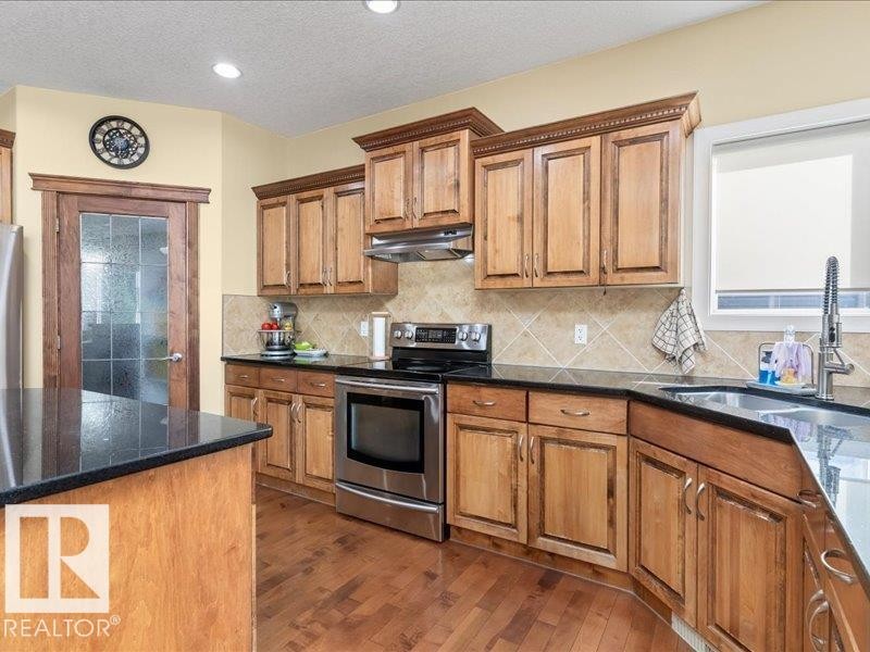Hardwood flooring, wood cabinetry with crown molding, stainless steel appliances, black countertops, and a tiled backsplash - 496 Ravine Court, Devon, AB