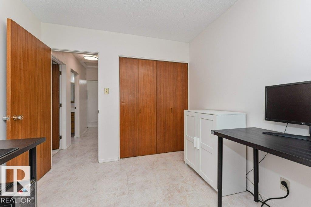 Well-lit room featuring light-colored tile flooring, white walls, and a wood-paneled closet with bi-fold doors - 11415 56 Avenue Nw, Edmonton, AB