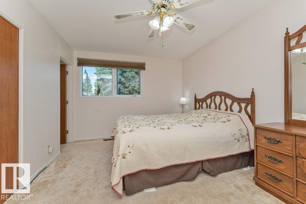 Carpeted bedroom with a built-in ceiling fan, window with exterior foliage, and a wood-finish door - 11415 56 Avenue Nw, Edmonton, AB