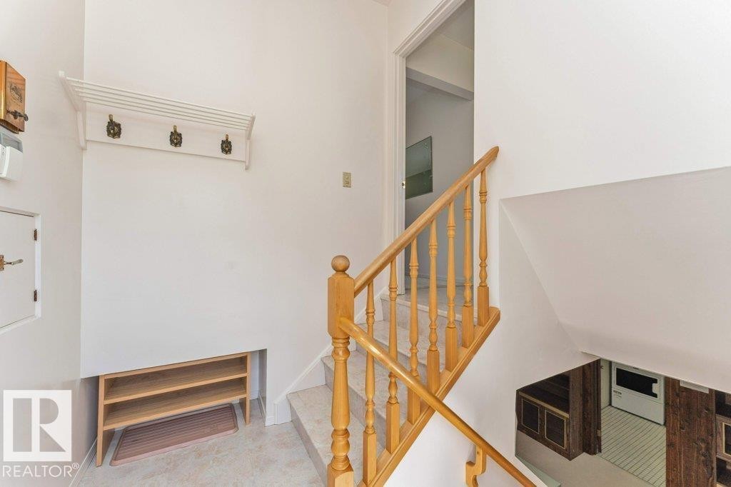 Bright entryway featuring a natural wood staircase with baluster railings and a built-in coat rack - 11415 56 Avenue Nw, Edmonton, AB