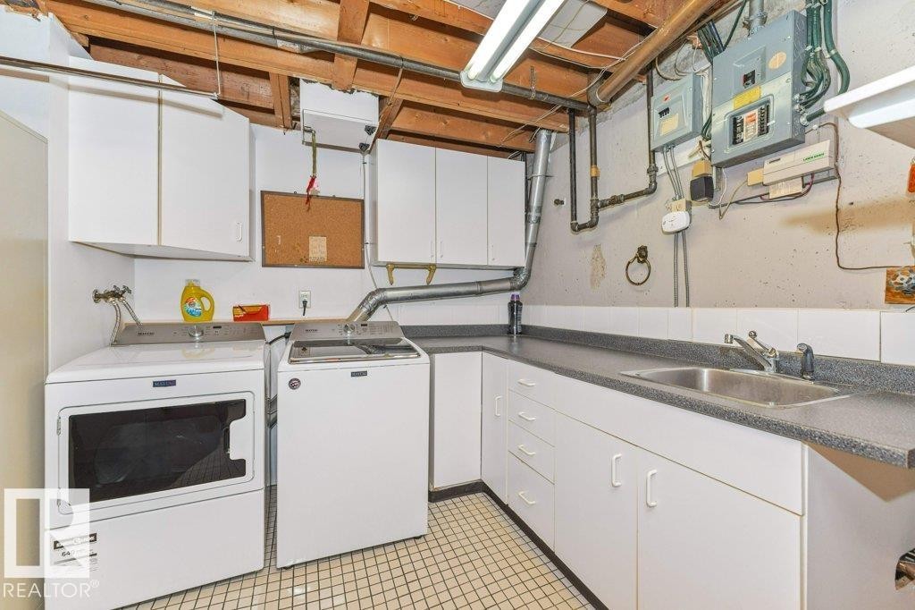 Laundry area featuring a utility sink, white base cabinetry with a dark countertop, white upper cabinetry, and a tiled floor - 11415 56 Avenue Nw, Edmonton, AB