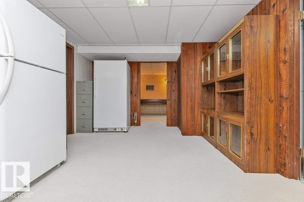 Finished basement space featuring wood-paneled walls, built-in display cabinetry with glass doors, and light-colored carpeting - 11415 56 Avenue Nw, Edmonton, AB