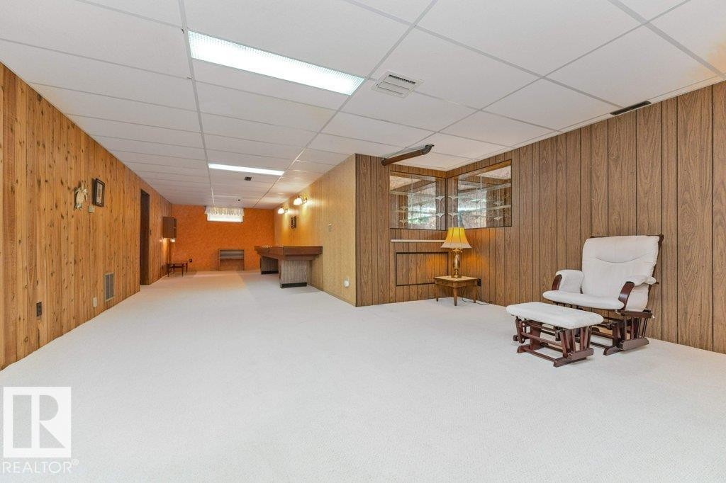 Expansive room featuring light-toned carpeting and wood paneling on the walls - 11415 56 Avenue Nw, Edmonton, AB
