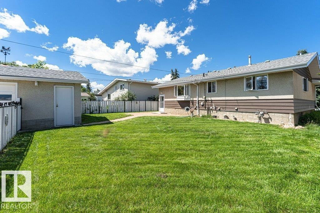 Expansive backyard with a manicured lawn, complete with a detached garage and a paved pathway - 11415 56 Avenue Nw, Edmonton, AB