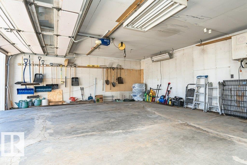 Spacious garage with an overhead automatic door opener, wall-mounted storage solutions, and concrete flooring - 11415 56 Avenue Nw, Edmonton, AB