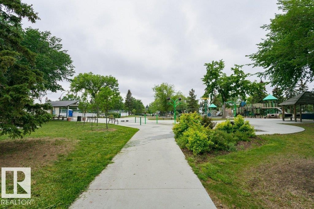 Expansive park grounds featuring a paved pathway, mature trees, and multiple play structures - 11415 56 Avenue Nw, Edmonton, AB
