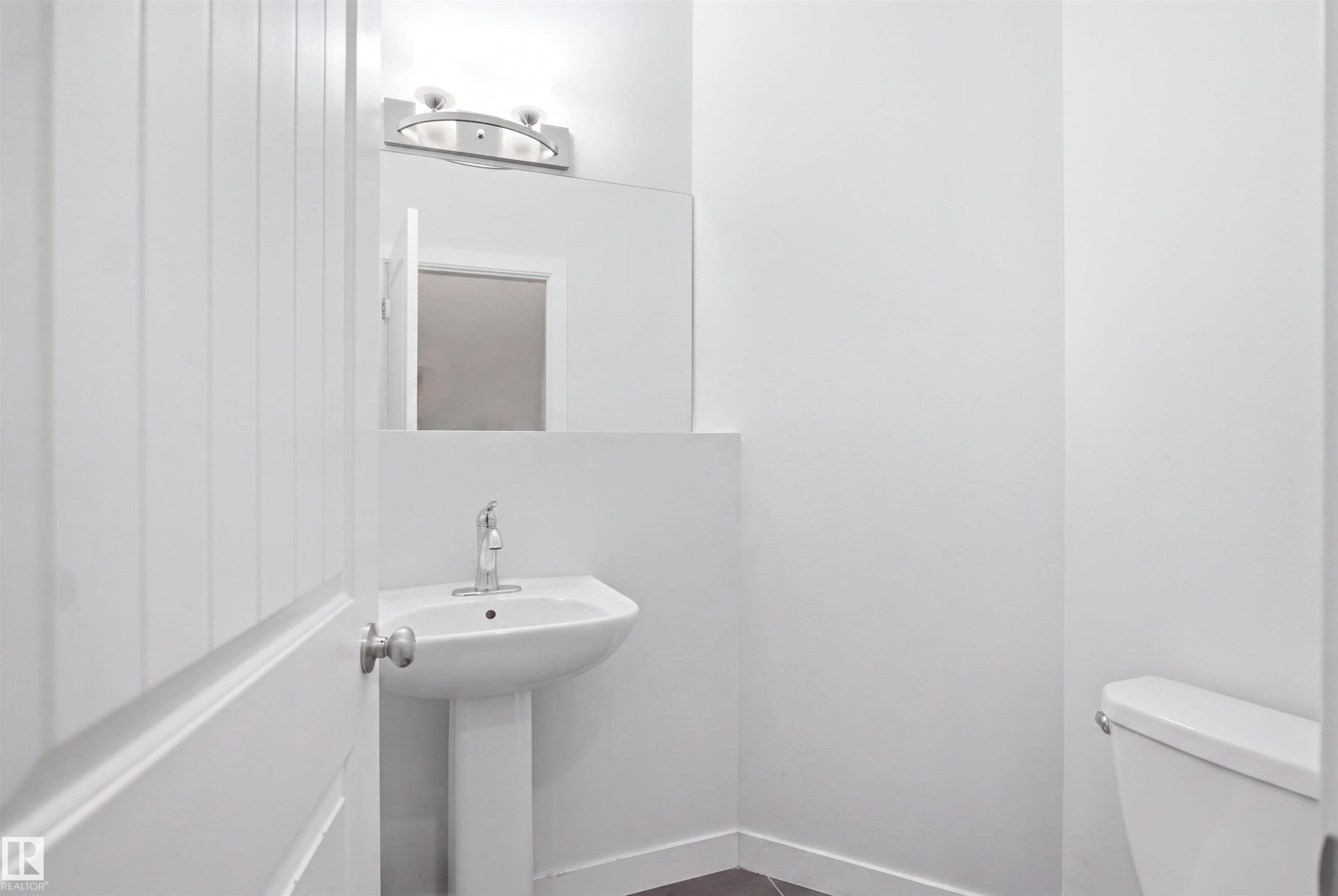 Pedestal sink with chrome faucet, mirror, wall-mounted light fixture, and white painted walls - #22 723 172 Street Sw, Edmonton, AB