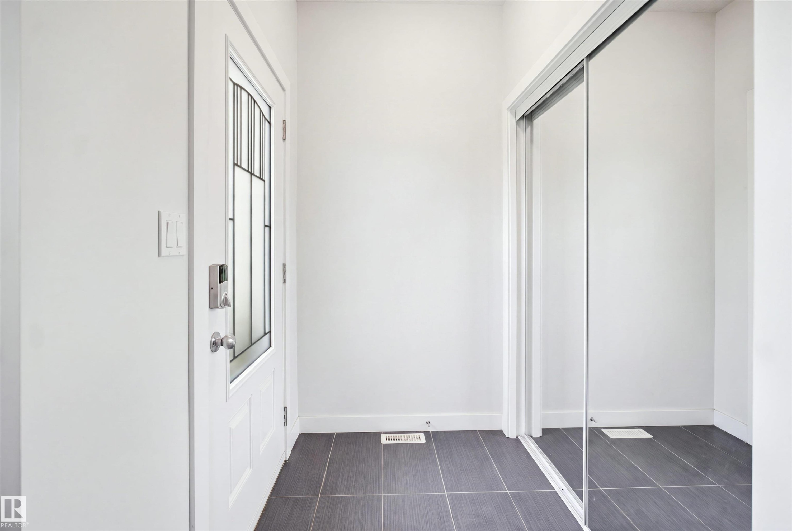 Entryway featuring a white door with decorative glass, a smart lock, dark tile flooring, and a mirrored sliding closet door - #22 723 172 Street Sw, Edmonton, AB