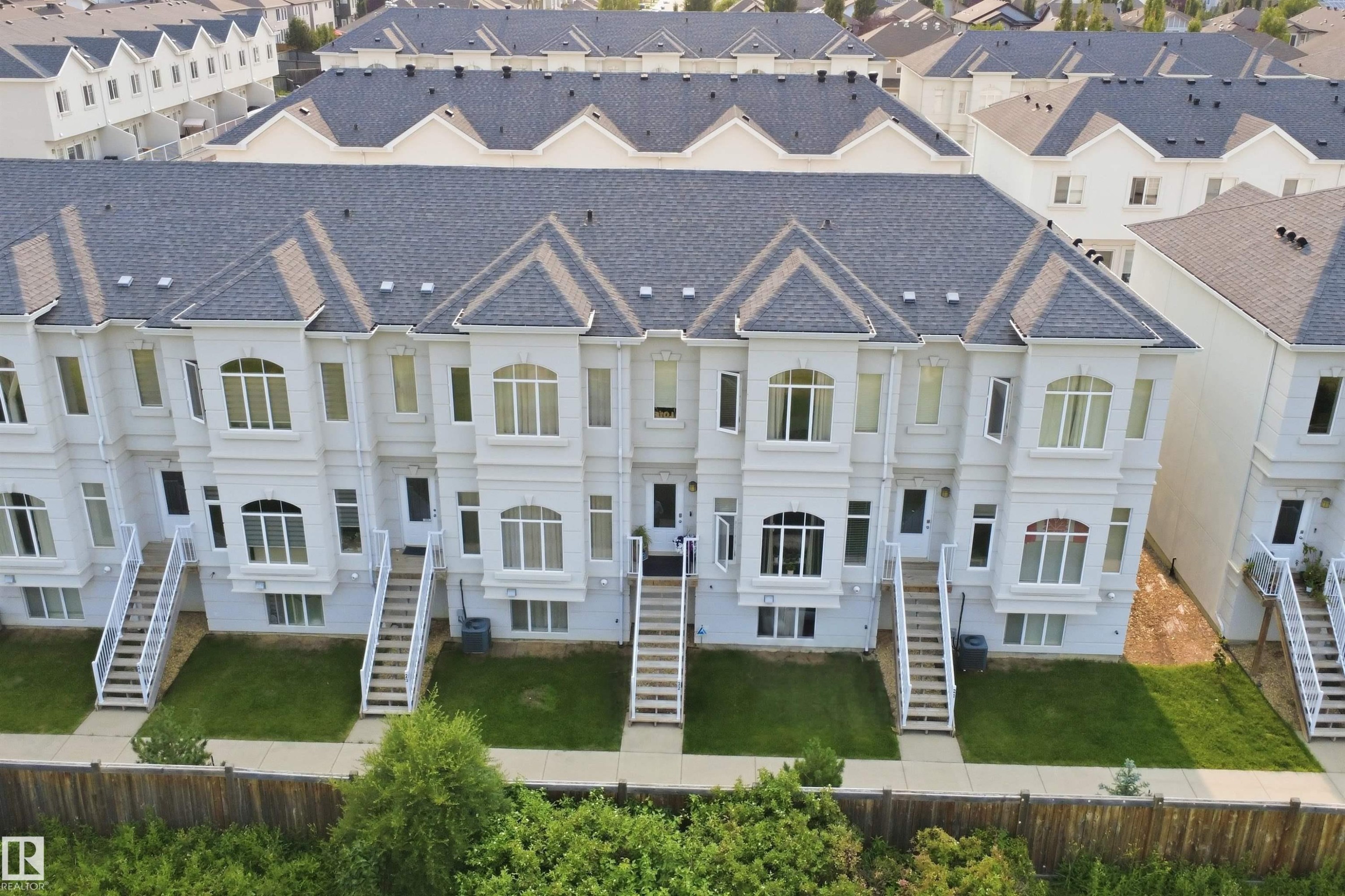 Townhome row featuring light-colored exteriors, multiple levels, prominent bay windows, and individual entry staircases - #22 723 172 Street Sw, Edmonton, AB