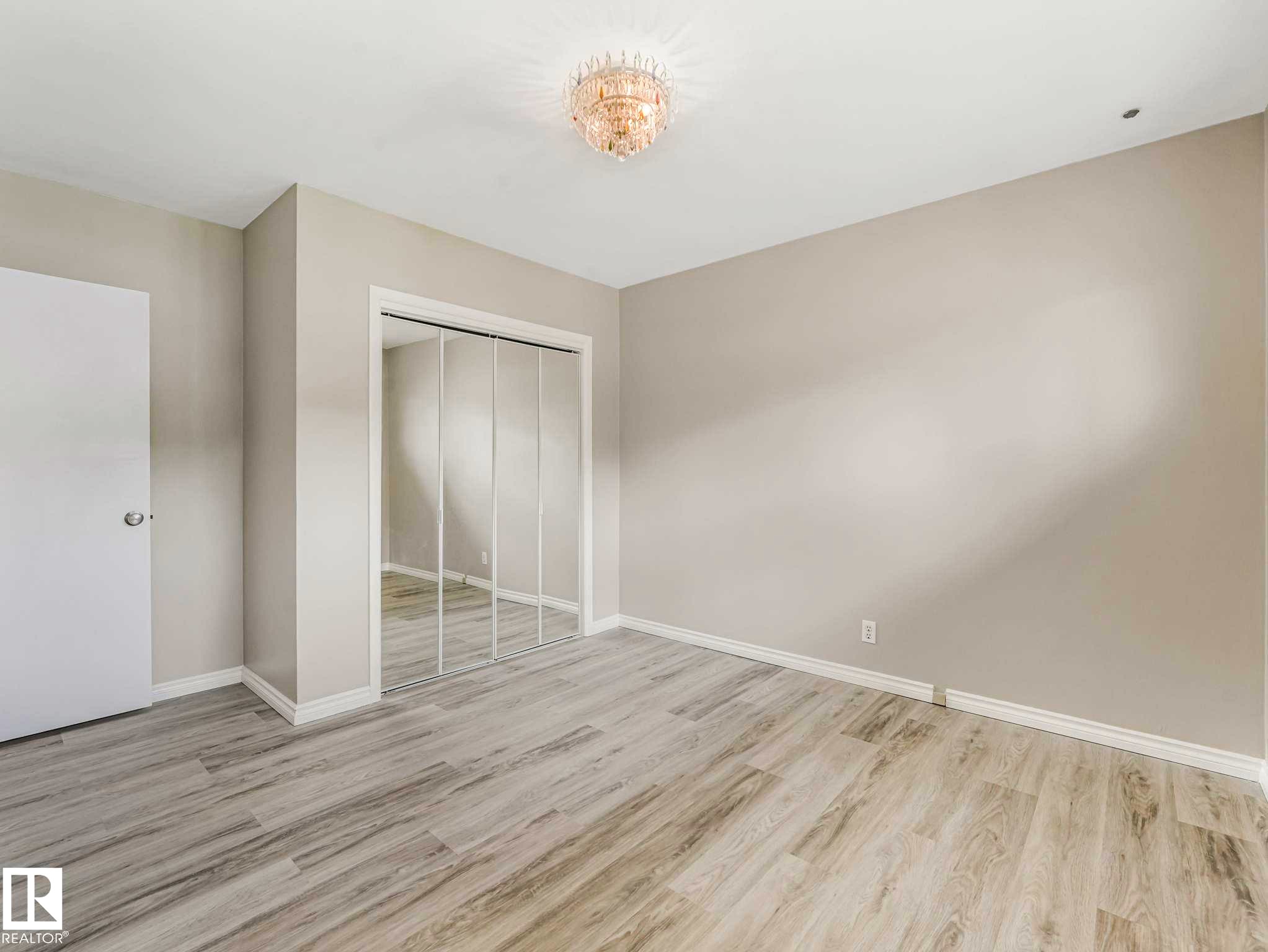 Light-colored wood-finish flooring, mirrored closet doors, and a decorative ceiling light fixture - 15916 88B Avenue Nw, Edmonton, AB