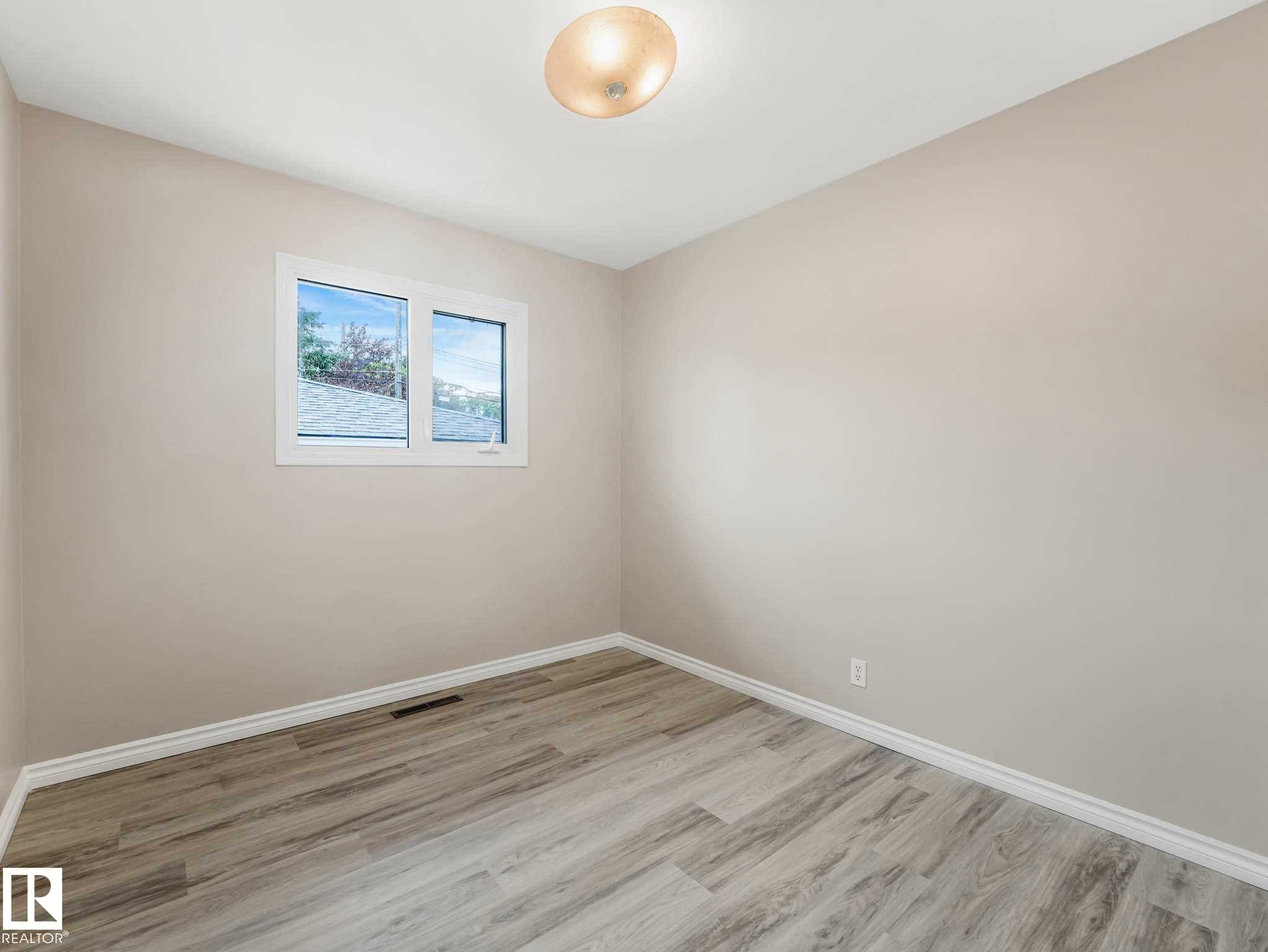 Neutral wall paint, wood-finish flooring, white window trim, and a flush mount ceiling light - 15916 88B Avenue Nw, Edmonton, AB