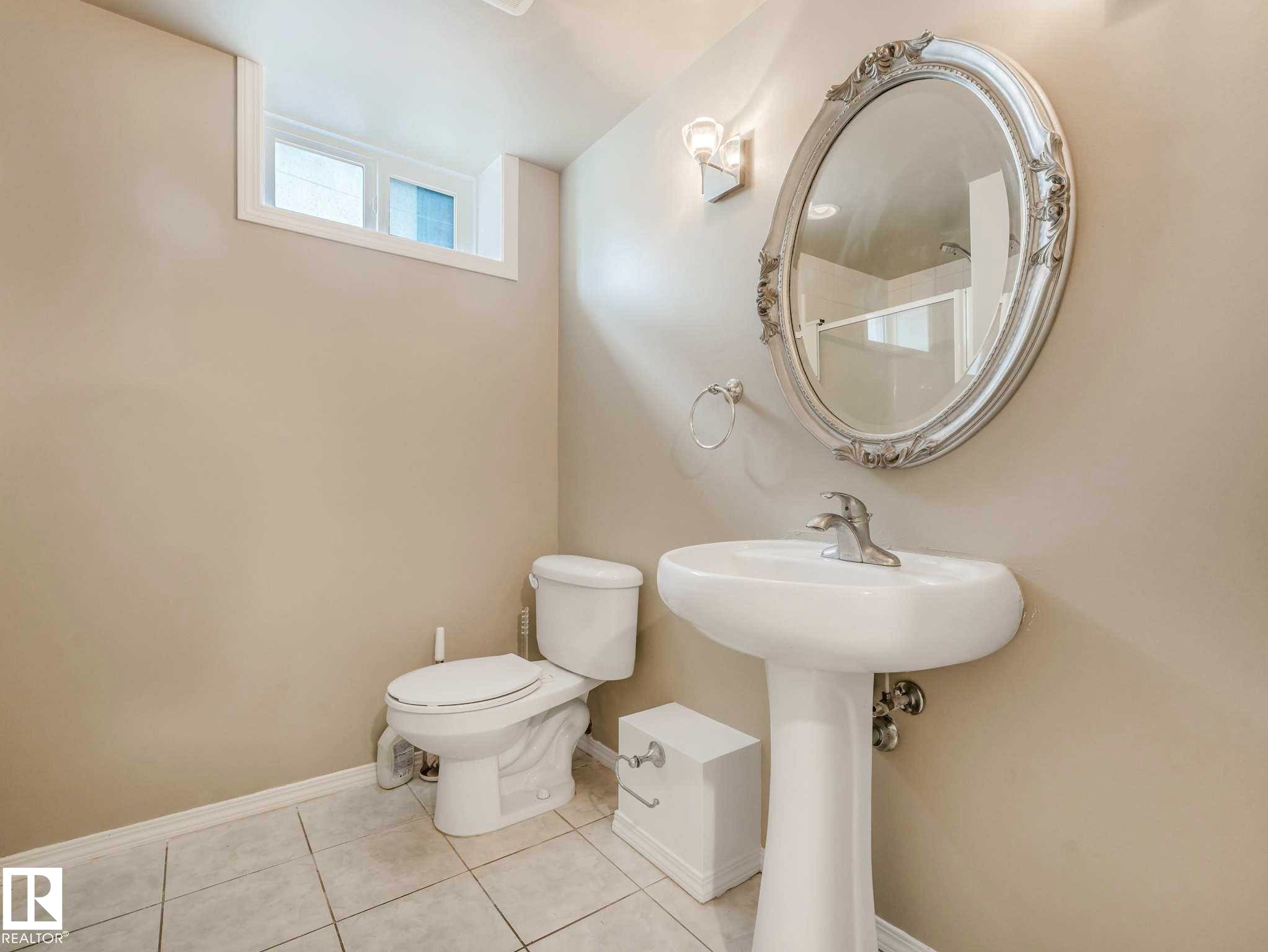 Pedestal sink with chrome faucet, oval mirror with ornate frame, and ceramic tile flooring - 15916 88B Avenue Nw, Edmonton, AB