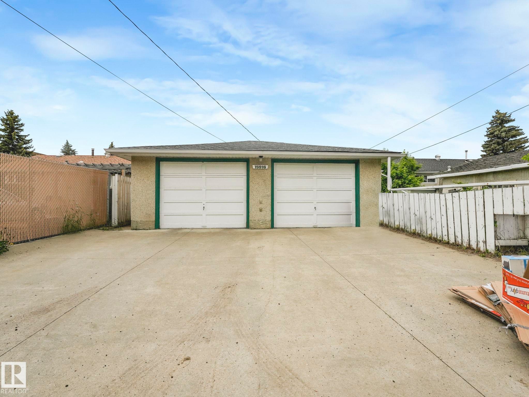 Two-car detached garage with white overhead doors, green trim, and stucco exterior - 15916 88B Avenue Nw, Edmonton, AB