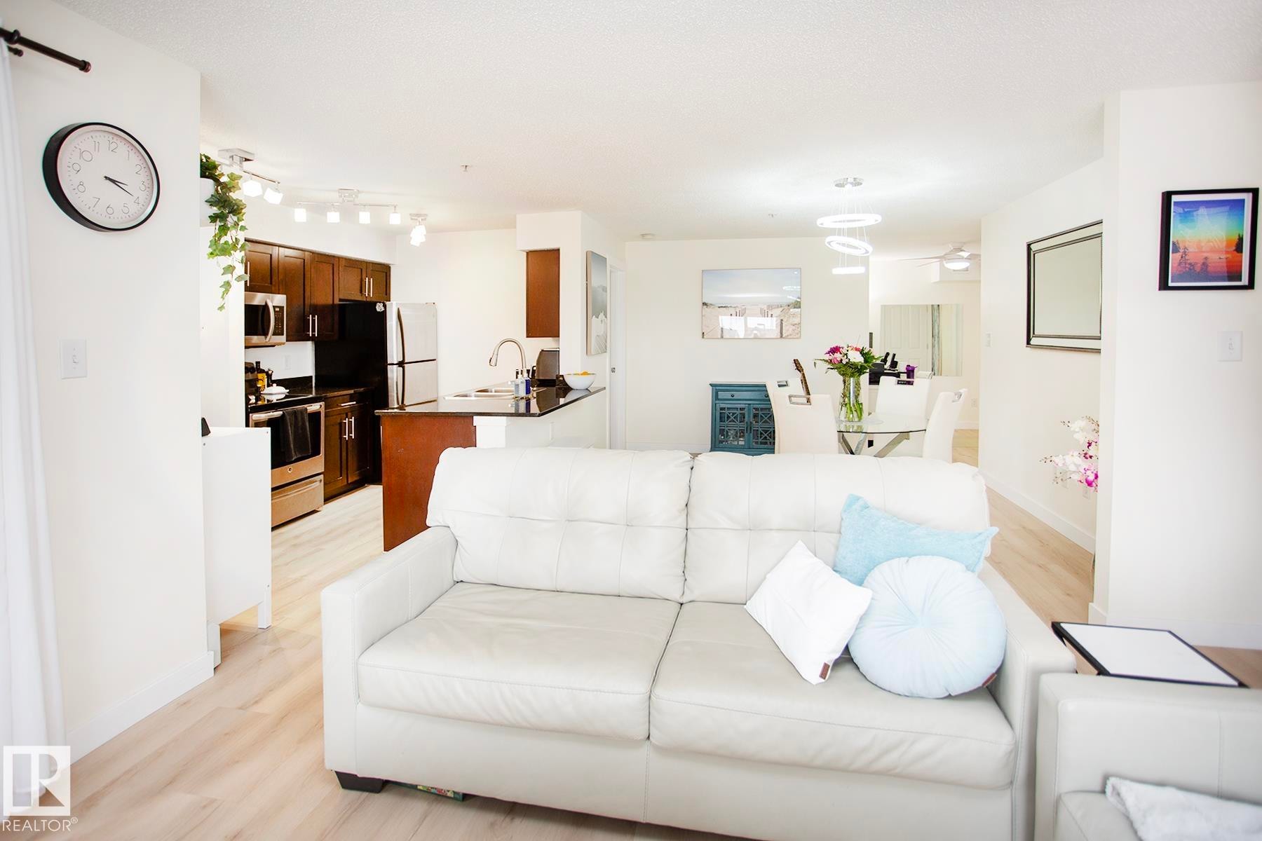 Open-concept living area with wood-finish flooring, recessed lighting, track lighting, and a modern kitchen featuring stainless steel appliances and dark wood cabinetry - #201 1070 Mcconachie Bv Nw, Edmonton, AB
