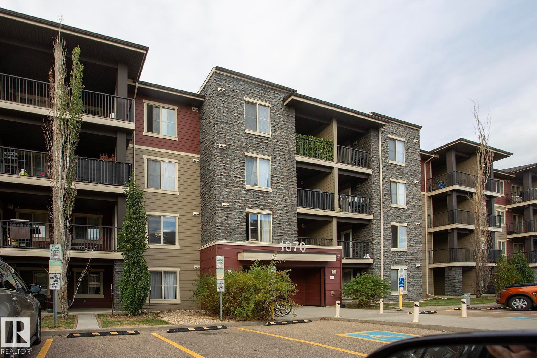 Multi-story residential building featuring stone veneer accents, multiple balconies with black railings, and a distinct entry canopy - #201 1070 Mcconachie Bv Nw, Edmonton, AB