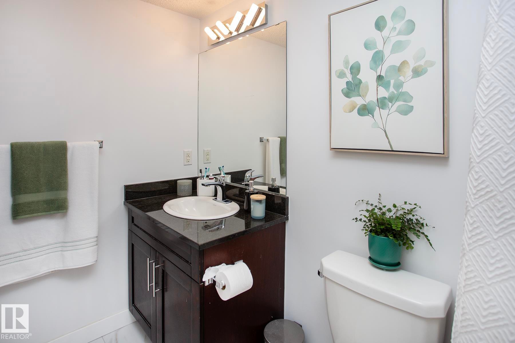 Vanity with a dark countertop and undermount sink, large wall-mounted mirror, and contemporary light fixture - #201 1070 Mcconachie Bv Nw, Edmonton, AB