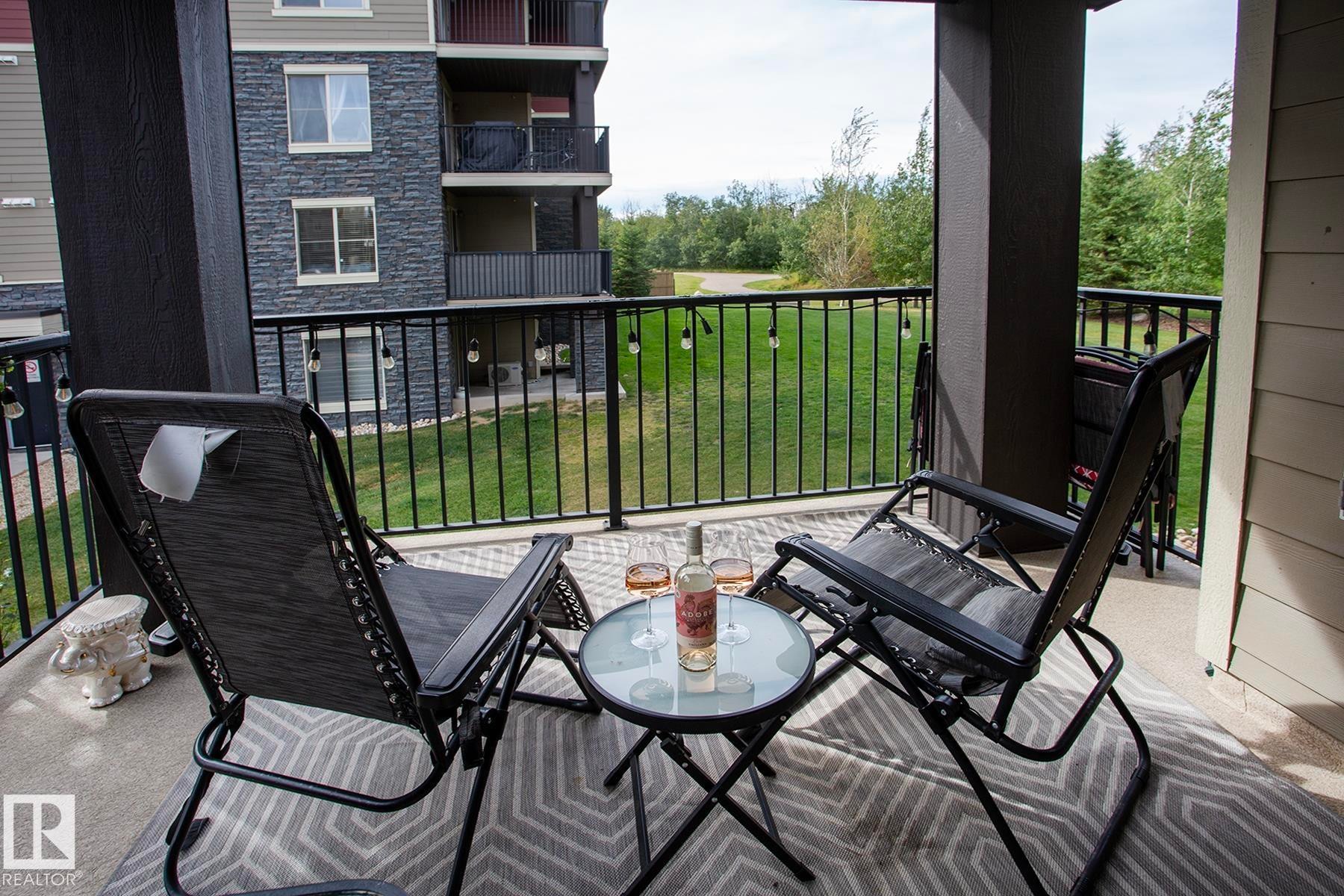 Covered outdoor patio with a concrete surface, black metal railings, and a green landscape beyond - #201 1070 Mcconachie Bv Nw, Edmonton, AB