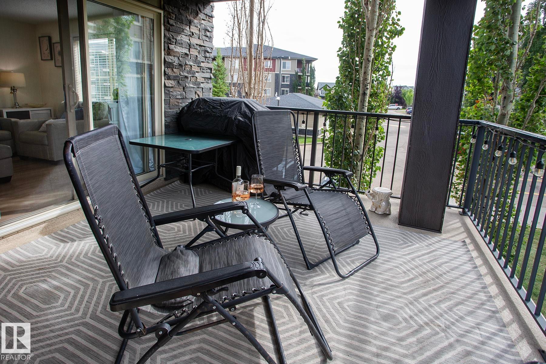 Private balcony with dark metal railings, stone accent wall, and sliding glass doors - #201 1070 Mcconachie Bv Nw, Edmonton, AB