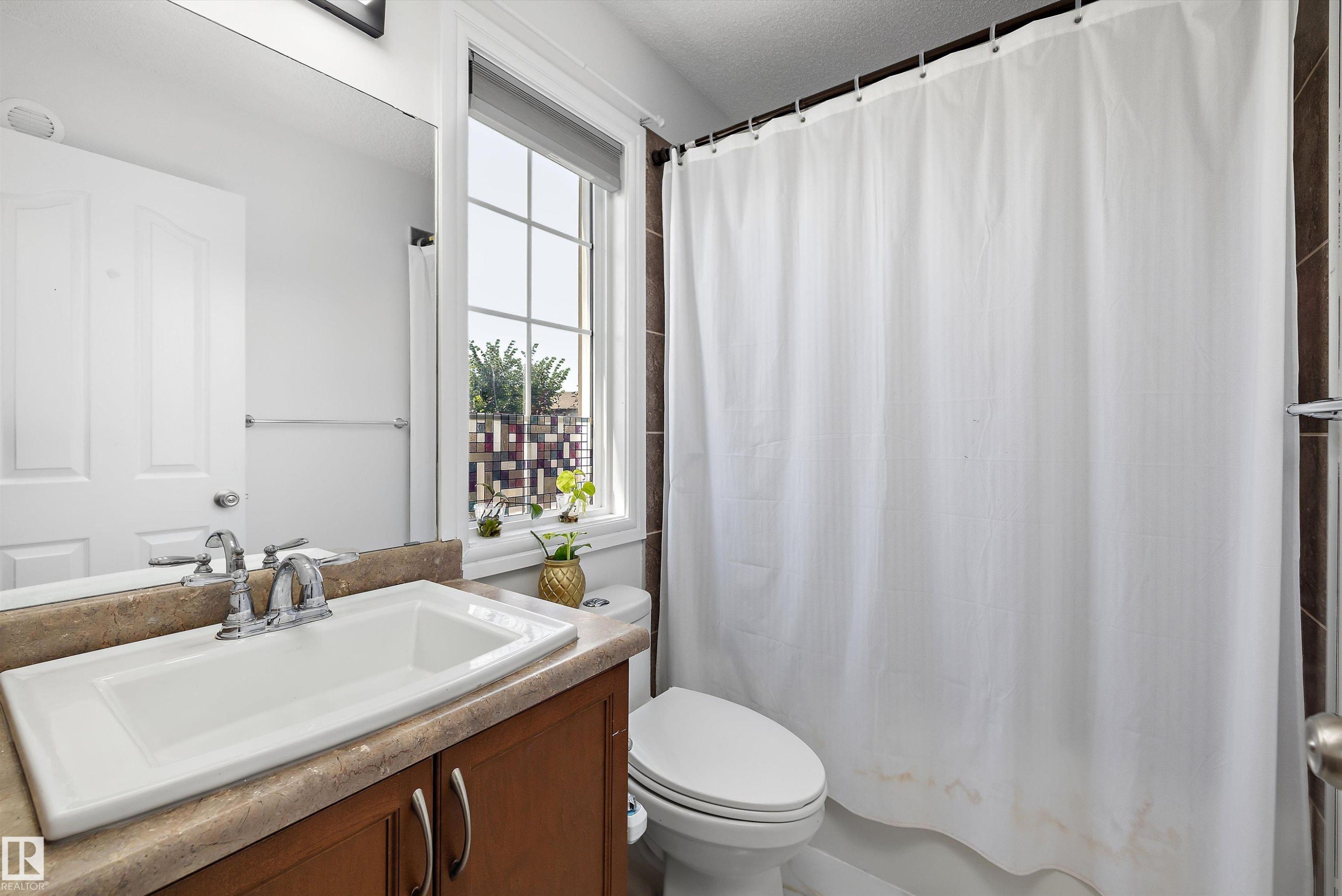 Bathroom featuring a window with grid detailing, wood-finish vanity with countertop, and an integrated white sink - 2803 12 Street Nw, Edmonton, AB