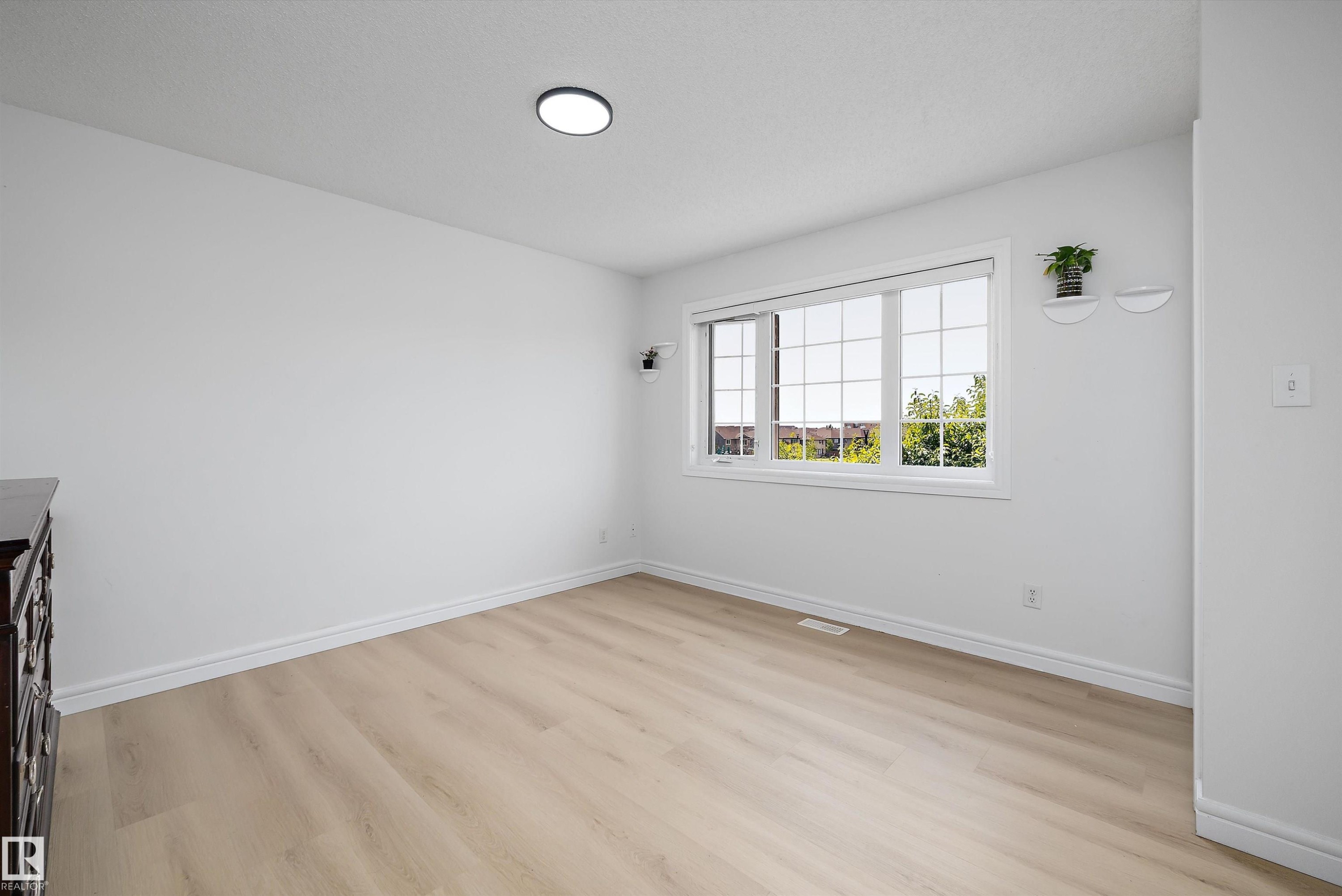 Light-filled interior featuring expansive window, wood-finish flooring, white baseboards, and a flush-mount ceiling light - 2803 12 Street Nw, Edmonton, AB